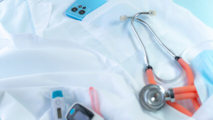 Smartphone with some medical tools and accessories, including a stethoscope, medical mask and electronic thermometer in medical coat pockets