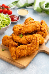 Chicken tenders served on a wooden board with salad and sauces