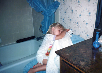 Adorable toddler child girl falls asleep on the toilet in the bathroom in the 1980s, circa 1987. Image is a vintage scan and may have imperfections