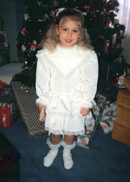 Circa 1990 - cute girl child dressed in white, by a Christmas tree. Image is a vintage scan and may have imperfections