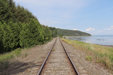 Fototapeta premium Railway in the countryside of Charlevoix in Quebec and in Canada. Summer landscape and horizon. Travel and destination and train transportation. Summer calendar with a view of a riverside.