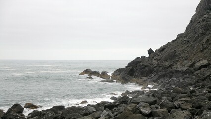 Rocky coastline meeting the ocean under cloudy sky