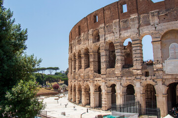 Side of the Roman Colosseum with Arches and Restoration Work in Rome.
Partial view of Roman Colosseum in Rome with visible arches, ruins, and trees on a sunny sum