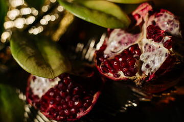Two juicy halves of a pomegranate are placed on a golden tray on a colored background near a green...