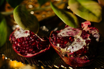 Two juicy halves of a pomegranate are placed on a golden tray on a colored background near a green...