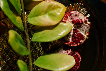 Two juicy halves of a pomegranate are placed on a golden tray on a colored background near a green...