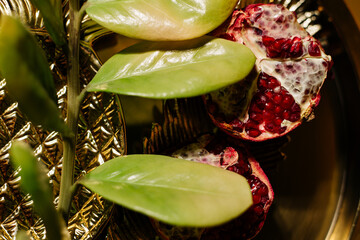 Two juicy halves of a pomegranate are placed on a golden tray on a colored background near a green...