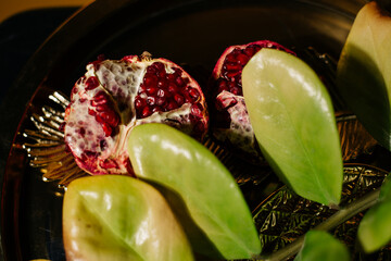 Two juicy halves of a pomegranate are placed on a golden tray on a colored background near a green...