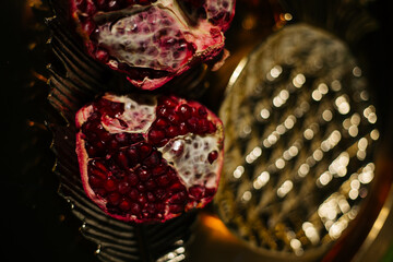 Two juicy halves of a pomegranate are placed on a golden tray on a colored background near a green...