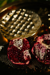 Two juicy halves of a pomegranate are placed on a golden tray on a colored background near a green...