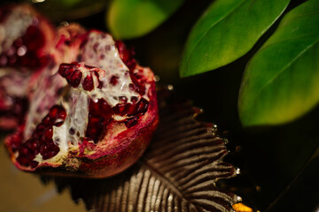 Two juicy halves of a pomegranate are placed on a golden tray on a colored background near a green...
