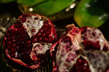 Two juicy halves of a pomegranate are placed on a golden tray on a colored background near a green...