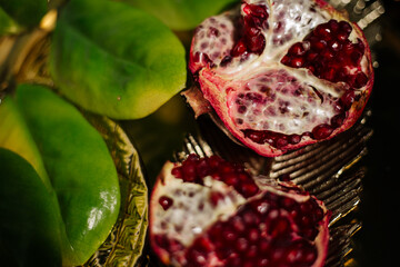 Two juicy halves of a pomegranate are placed on a golden tray on a colored background near a green...