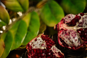 Two juicy halves of a pomegranate are placed on a golden tray on a colored background near a green...
