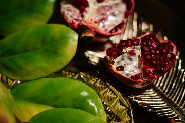 Two juicy halves of a pomegranate are placed on a golden tray on a colored background near a green...