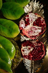 Two juicy halves of a pomegranate are placed on a golden tray on a colored background near a green...