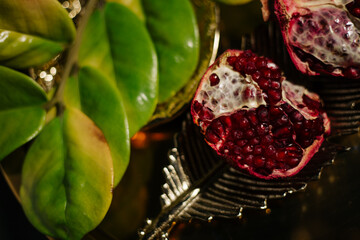 Two juicy halves of a pomegranate are placed on a golden tray on a colored background near a green...