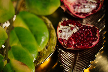 Two juicy halves of a pomegranate are placed on a golden tray on a colored background near a green...