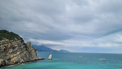 Coastal view of Crimea with rocky cliffs and turquoise sea under a cloudy sky. Boats are visible in the distance, creating a serene atmosphere.