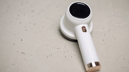 A modern fluff remover with a sleek white design and a black circular top. It is placed on a light-colored fabric surface, showcasing its practical use for removing lint. copy space