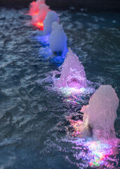 Colorful water fountain with illuminated jets in a pool. The water creates a vibrant display with...