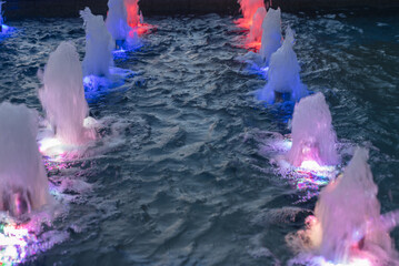 Colorful water fountains illuminated at night, creating a vibrant display in a pool. The scene...