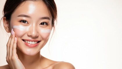 Young beautiful Asian woman with bright smile applies face cream. Korean spa skincare banner shows clear, glowing complexion. Healthy, happy model promoting natural beauty, fresh makeup.