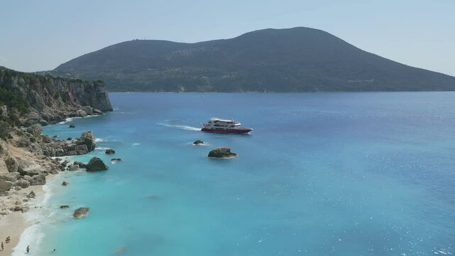 A scenic view of a sandy beach on Ithaki island, Greece. People are swimming and relaxing under the sun while a large cruise ship anchors nearby in the turquoise sea. Perfect summer travel atmosphere.