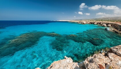 turquoise waters near ayia napa cyprus with darker patches indicating underwater features a rugged rocky shoreline is visible in the upper right corner