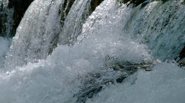 CLOSE UP, SLOW MOTION: Crystal clear water splashes over cascading rocks submerged in a wild, free flowing river. Vibrant motion and textured natural patterns of the turbulent flow in river rapids.