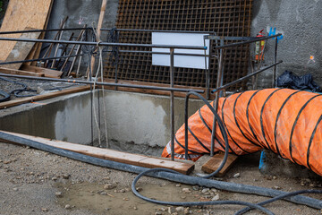 Rectangular concrete pit on construction site with flexible orange air duct entering the shaft....