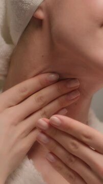Happy beautiful Caucasian young woman applying body cream rubbing neck skincare gorgeous female model in bath towel bathrobe apply lotion cosmetic massaging soft skin care beauty routine home bathroom
