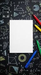 Blank card blank paper on chalkboard with math equations and colorful markers surrounding it overhead shot