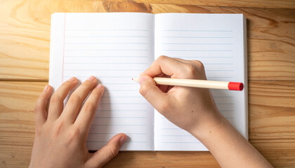 Child’s Hand Holding Pencil, Practicing Writing on Lined Notebook, Top View in Morning Light