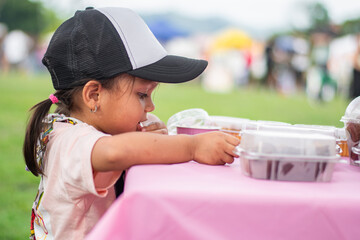 Side view of three-year-old Colombian girl interacting with pastries at children’s entrepreneurship fair
