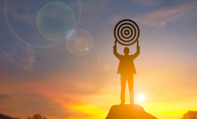 Silhouette of businessman holding target board on the top of mountain