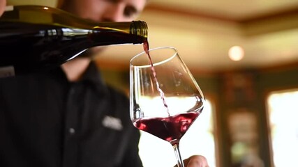 A man pouring red wine from a bottle into a clear glass in a warm lit environment - Powered by Adobe