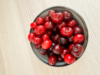 Freshly harvested cherries in a black bowl on a wooden table