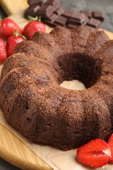 Tasty bundt cake, chocolate pieces and strawberries on grey table, closeup
