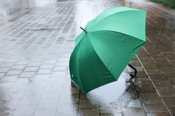 Green umbrella on wet asphalt under heavy rain, space for text