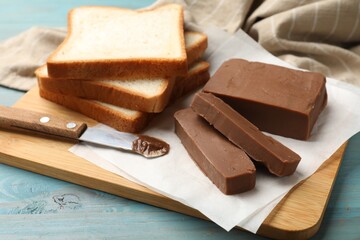 Pieces of tasty chocolate butter, slices of bread and knife on light blue wooden table, closeup