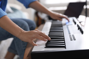 Woman working with MIDI keyboard at table indoors, closeup