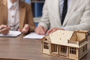 Real estate agent working with client at desk in office, focus on house model