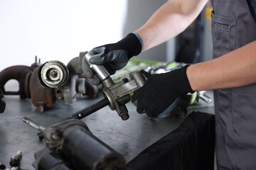 Auto parts. Professional mechanic fixing manual transmission at grey table indoors, closeup