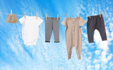 Different baby clothes drying on washing line against blue sky