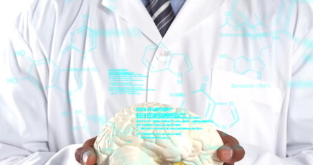 Researcher in lab coat and tie holding brain model in studio, with Serotonin molecular overlays