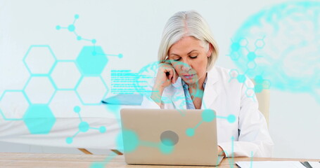 Analyzing data doctor wearing white coat viewing laptop at desk in exam room with teal overlays