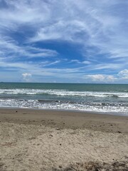 A serene beach scene with gentle waves rolling onto the sandy shore, under a beautiful blue sky with scattered clouds.