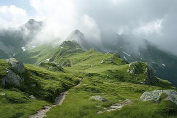 A winding dirt path leading through lush green mountainous terrain with large rocks and misty clouds partially covering rugged mountain peaks under a cloudy sky