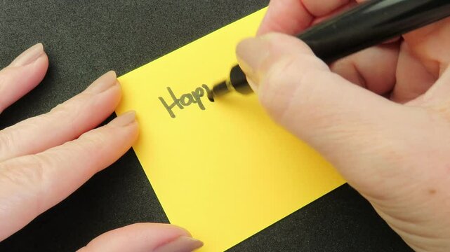 Closeup video of woman hands writing the expression "Happy Teacher's Day" with a smile on an orange note. Writing a Happy Teacher's Day card.